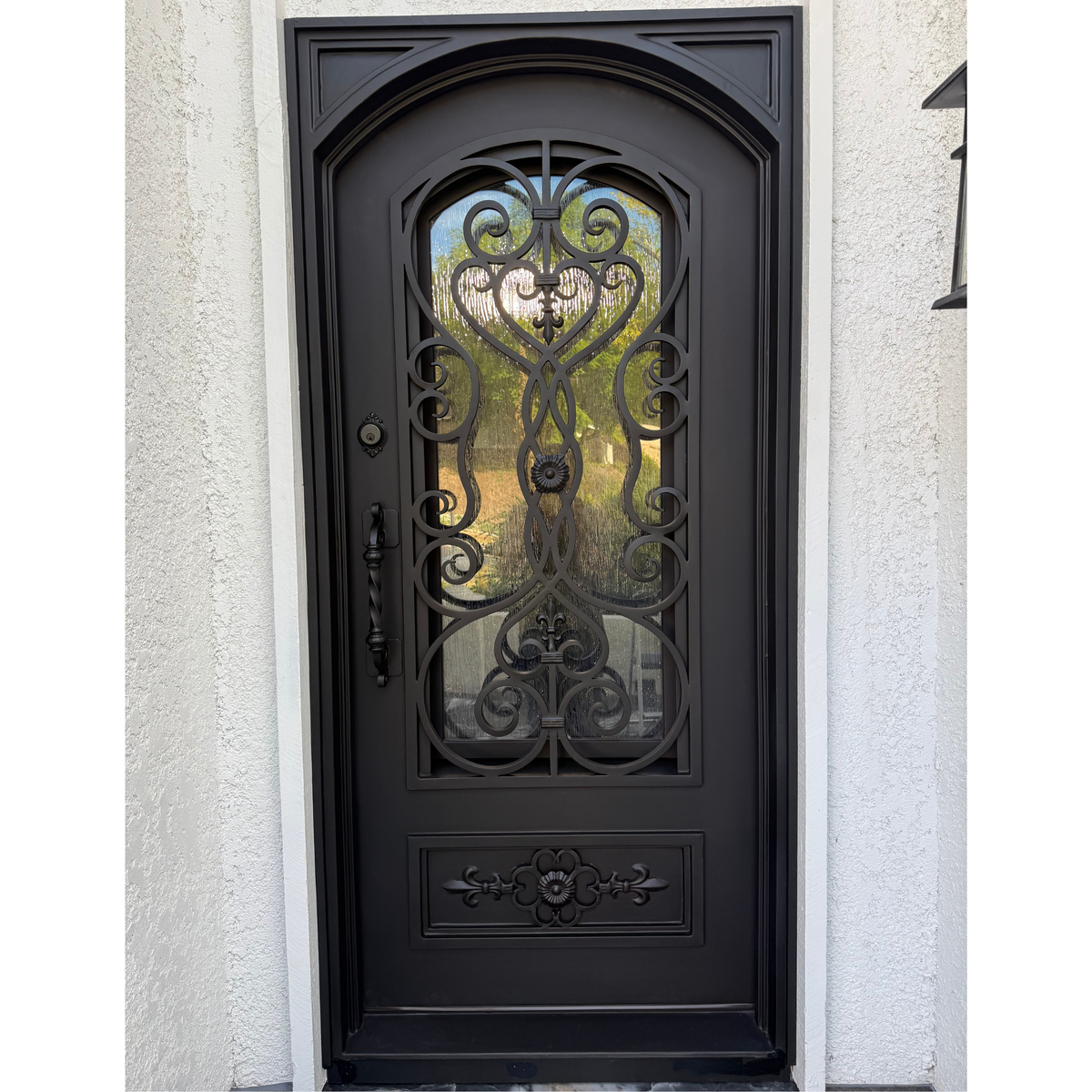 Decorative black wrought iron door with glass panels on a light gray wall.
