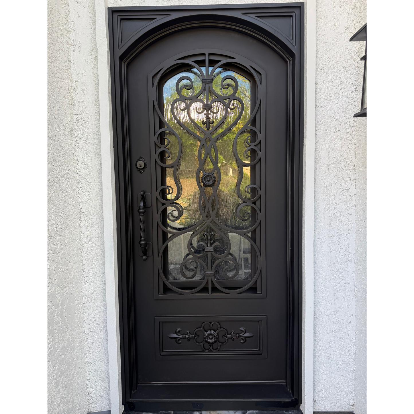 Decorative black wrought iron door with glass panels on a light gray wall.